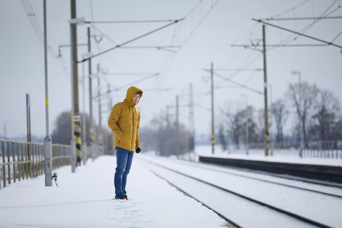 Podróżny w żółtej kurtce czeka na zaśnieżonym peronie kolejowym